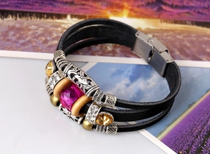 Détail d'un bracelet en cuir multicouche avec cristal magenta et breloques vintage