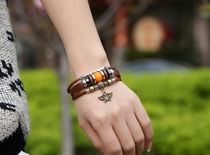 Detail of multi-layer leather bracelet with orange bead and bronze butterfly charm