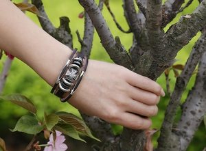 Detail of multi-layer brown leather bracelet featuring a silver Maltese cross charm