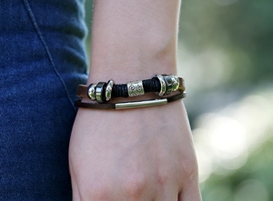 Detail of layered leather bracelet with silver metal beads worn on wrist with denim cloth
