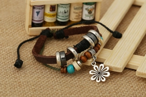 Dettaglio di un bracciale multistrato in pelle con ciondolo a fiore e perla turchese