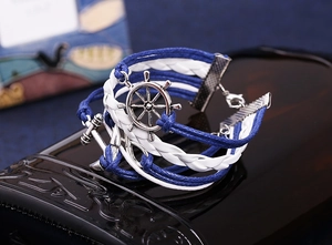 Detail view of multilayer braided leather bracelet with silver anchor and helm charms