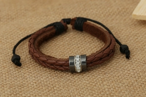 Close-up of woven brown leather bracelet with rhinestone metal charms on linen background