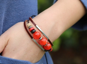 Detail of a multi-layer dark brown leather bracelet with red beads on a woman's wrist