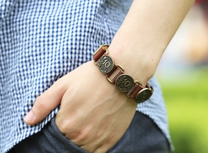 Close-up of vintage brown leather bracelet with bronze French coin charms on male wrist