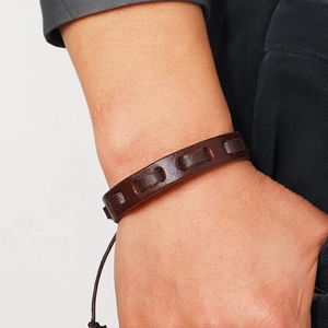 Close-up of a woven dark brown leather bracelet with adjustable cords on a male wrist