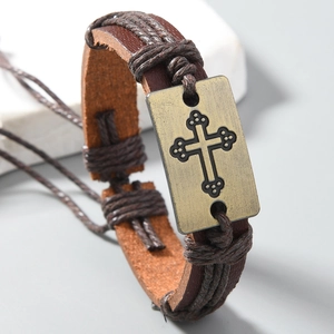 Détail d'un bracelet en cuir tressé avec plaque de croix en bronze vintage et lanière