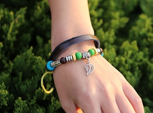 Detail of bohemian leather bracelet with colorful wooden beads and a metallic leaf charm