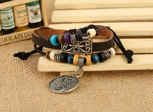 Detail view of multi-layer leather bracelet with beads and Yin Yang charm on wood