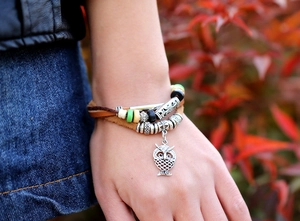 Dettaglio del bracciale multistrato in pelle con ciondolo a gufo indossato all'aperto