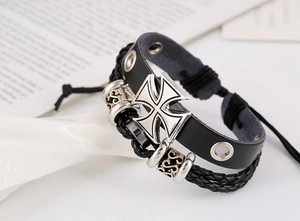 Détail d'un bracelet multicouche en cuir avec une breloque croix de malte argentée vintage