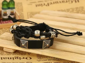 Detail of punk style black leather bracelet set with silver metal charms on retro newsprint