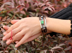 Multi-layer woven leather bracelet with metal beads and green thread detail on model wrist