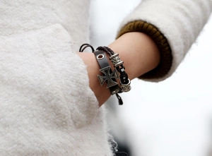 Gros plan sur les bracelets en cuir noir et corde tressée avec un pendentif en croix argentée