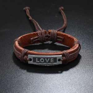 Macro detail of hand-woven leather bracelet featuring vintage silver LOVE engraved plate
