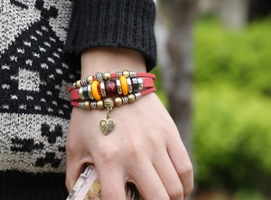 Close-up of red leather wrap bracelet with colorful beads and a heart-shaped floral charm
