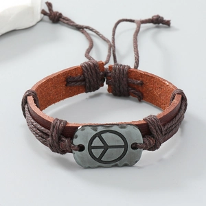 Dettaglio del bracciale in pelle marrone con placca in metallo vintage e simbolo della pace