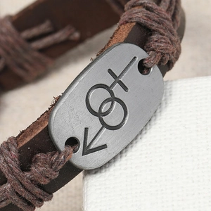 Macro detail of brown leather braided bracelet with an engraved vintage metal charm