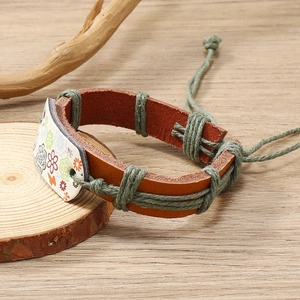 Handmade leather floral bracelet with adjustable woven cord on vintage wooden background