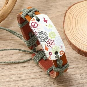 Detail of handmade woven leather bracelet with colorful floral and peace sign charms