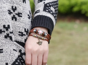 Dettaglio di bracciale in pelle multistrato con perline di ceramica e ciondolo a farfalla