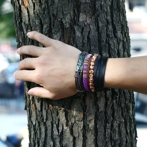 Detail of layered leather bracelets featuring an alloy leaf charm and ethnic woven textures