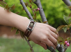 Close-up of a men's vintage brown multi-layer leather bracelet with an iron cross charm