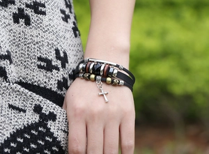 Detail of multilayer leather bracelet featuring vintage silver cross and wooden beads