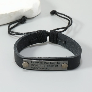 Macro shot of black leather bracelet with engraved metal plate and braided cord