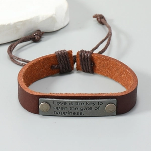Detail of vintage brown leather bracelet with engraved inspirational metal plate and cord