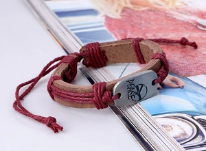 Detail of woven leather bracelet featuring a metal plate engraved with PEACE and peace symbol