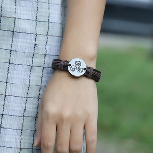 Close-up of vintage leather bracelet with triskelion charm on wrist in natural light