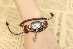 Detail view of vintage leather wrap watch with woven cord and bronze leaf charm