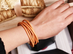 Detail of multi-strand orange cowhide leather bracelet worn on wrist with layered look