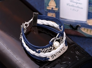 Close-up of multilayer braided bracelet with silver wings, infinity symbol and Believe plate