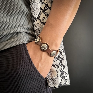 Macro detail of men's brown leather bracelet featuring silver spade Ace charms and snaps