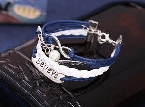 Macro detail of braided multi-layer bracelet with silver wings and Believe metal charm