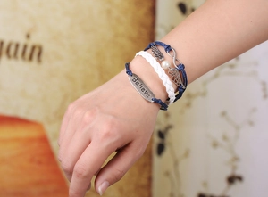 Detail of woven bracelet with wings, infinity symbol, and engraved Believe charm