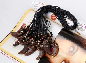 Macro view of eagle head carving and wolf tooth pendant on black wax rope with wood beads
