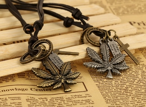 Macro detail of vintage maple leaf pendant with cross on adjustable brown leather cord