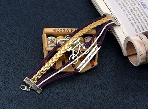 Détail d'un bracelet en cuir multicouche avec breloque vélo et plaque gravée inspirante