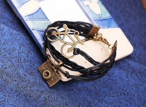 Détail du bracelet en cuir tressé multicouche avec breloques vélo et appareil photo