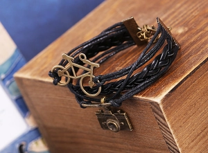 Gros plan d'un bracelet en cuir tressé vintage avec charmes vélo et appareil photo
