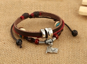 Dettaglio del bracciale multistrato in pelle con ciondolo a teschio su sfondo di juta