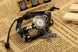 Detail of vintage bronze watch with black leather straps and butterfly charm on newsprint