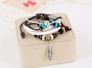 Macro detail of bohemian leather bracelet featuring wooden beads and silver feather pendant