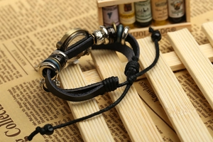 Macro shot of vintage black leather wrap watch with bronze charms on a retro paper backdrop