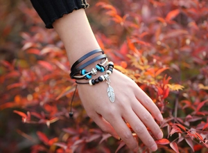 Detail of bohemian layered leather bead bracelet with a silver feather charm and turquoise beads