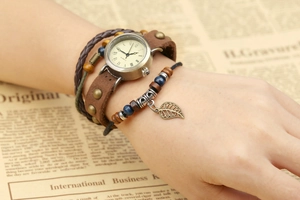 Close-up of vintage quartz watch with brown leather layers and a leaf pendant detail