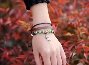 Close-up of a handmade leather owl charm bracelet with layered beads and woven strands